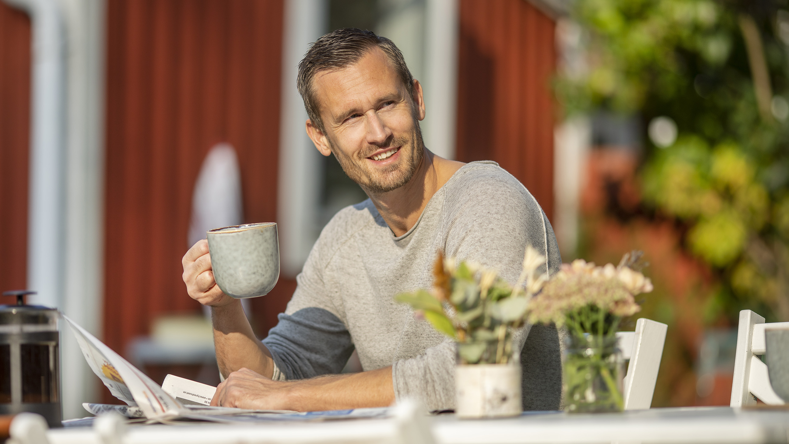 En man sitter utomhus och dricker en kopp kaffe. 