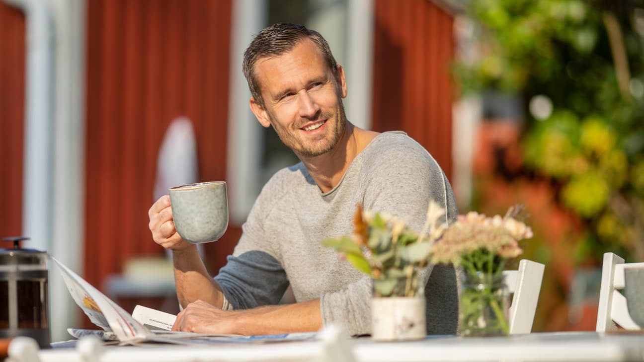 En man sitter utomhus och dricker en kopp kaffe. 