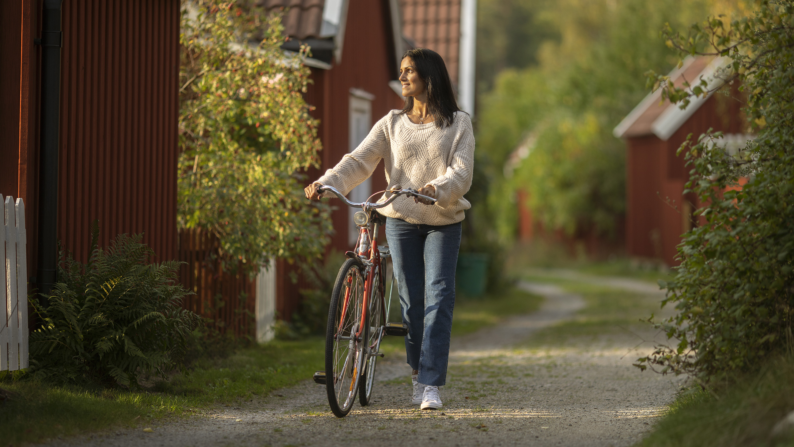 En kvinna leder sin cykel på en grusväg. 