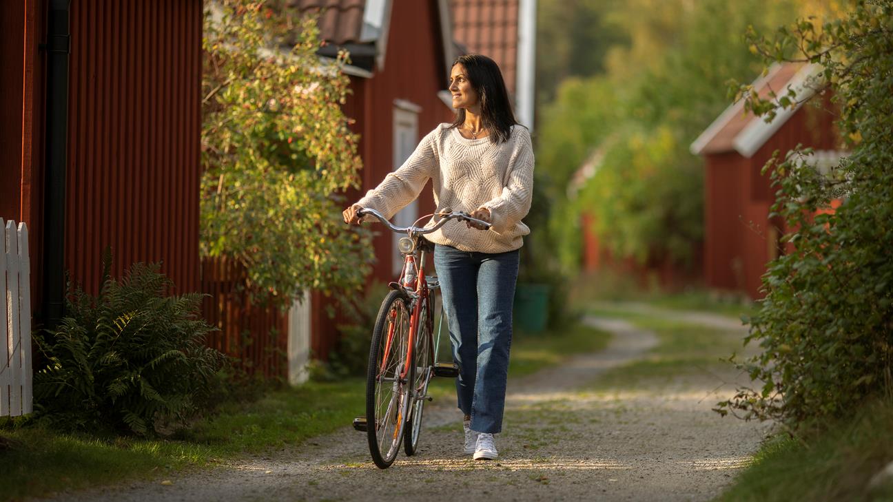 En kvinna leder sin cykel på en grusväg. 