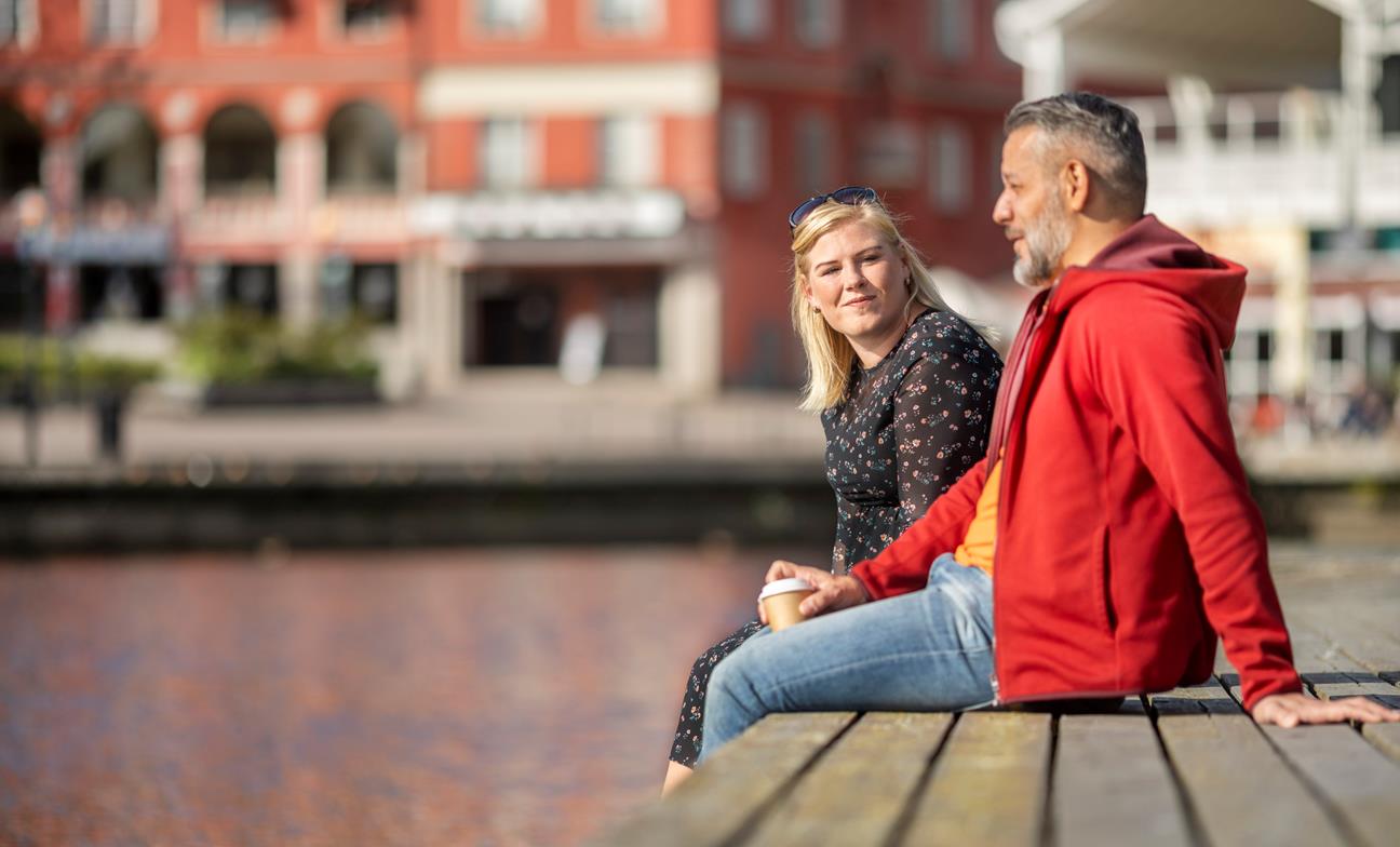 En man och en kvinna sitter bredvid varandra på en brygga vid vattnet. 