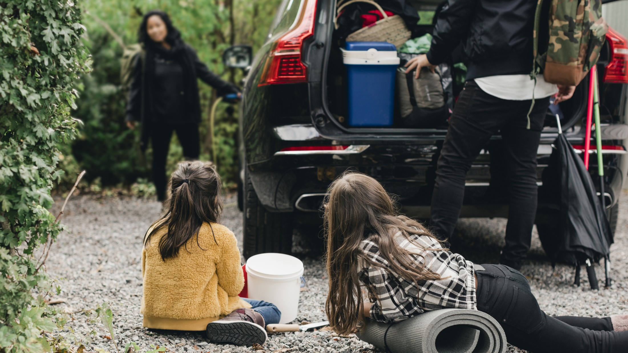 Bild på en familj som håller på att packa in sig i en bil parkerad under ett träd.